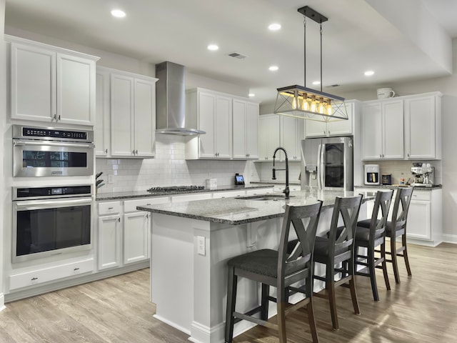 kitchen featuring appliances with stainless steel finishes, wall chimney exhaust hood, and white cabinetry