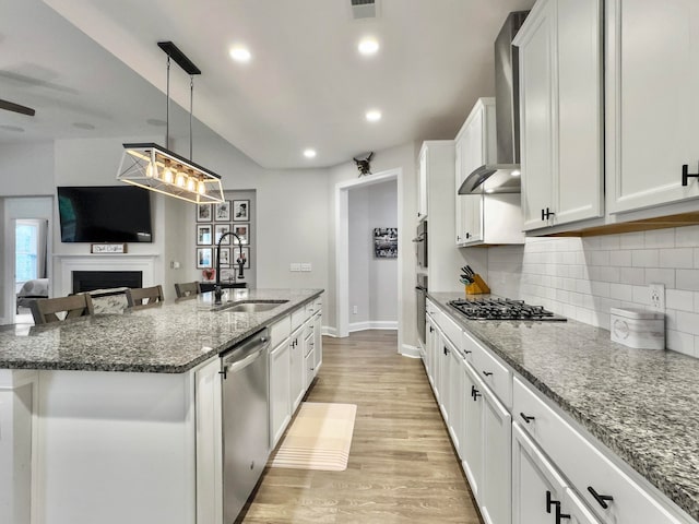 kitchen with sink, decorative light fixtures, a kitchen island with sink, wall chimney range hood, and appliances with stainless steel finishes