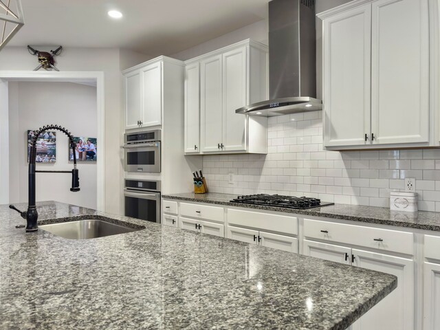 kitchen with stainless steel appliances, wall chimney exhaust hood, sink, and white cabinetry