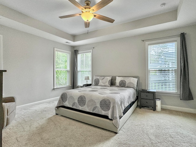 carpeted bedroom with multiple windows, a tray ceiling, and ceiling fan