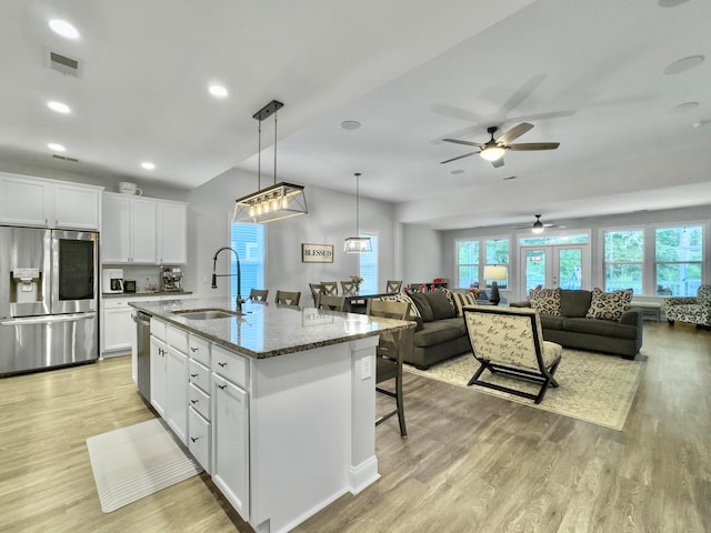 kitchen with light stone countertops, stainless steel appliances, ceiling fan, a center island with sink, and sink