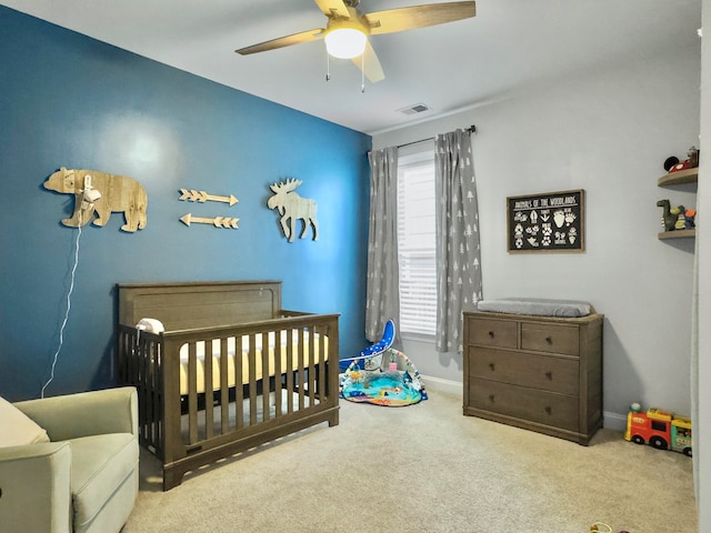 carpeted bedroom featuring ceiling fan and a nursery area