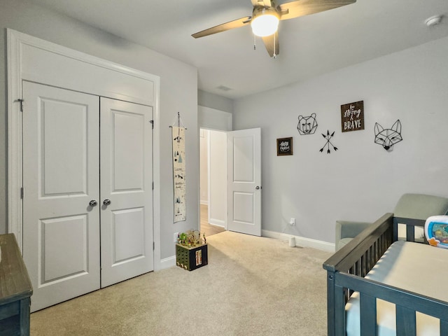 carpeted bedroom with ceiling fan, a crib, and a closet