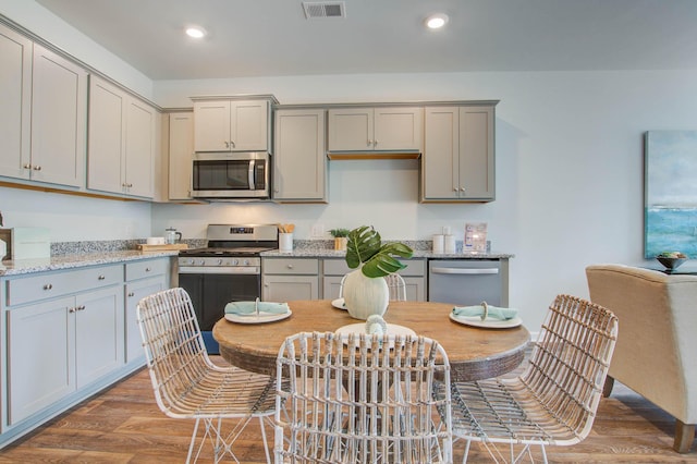 kitchen featuring light stone counters, gray cabinetry, stainless steel appliances, wood finished floors, and visible vents