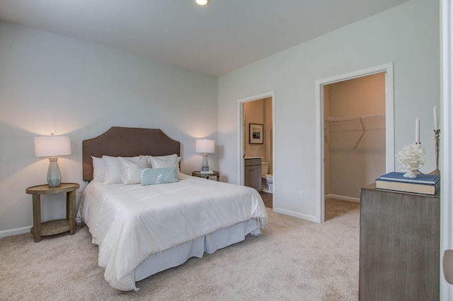 bedroom with light carpet, baseboards, a spacious closet, a closet, and ensuite bath