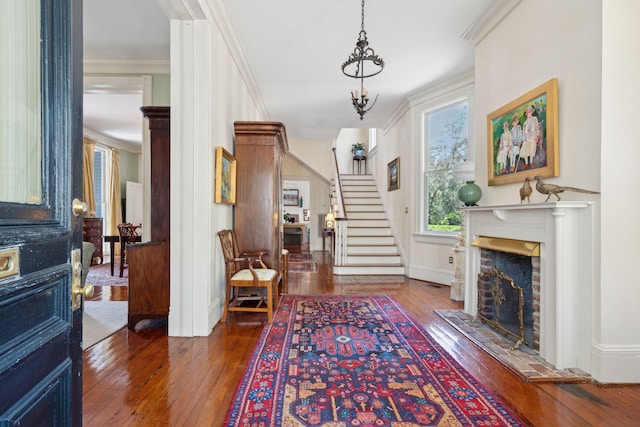 foyer featuring stairway, ornamental molding, hardwood / wood-style floors, and a fireplace with raised hearth