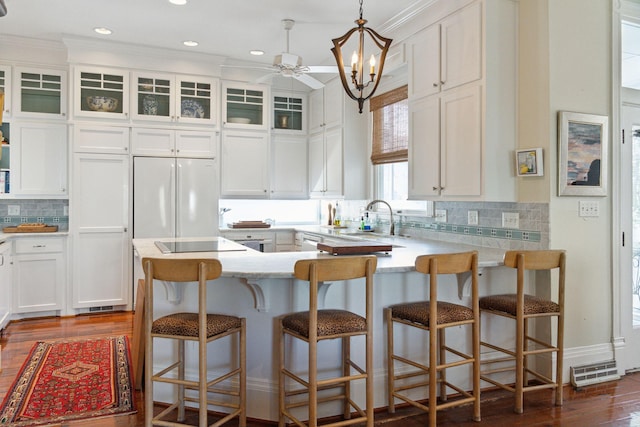 kitchen featuring a peninsula, freestanding refrigerator, white cabinets, dark wood-type flooring, and ornamental molding