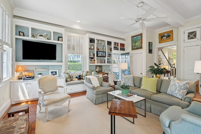 living area with ceiling fan, wood finished floors, ornamental molding, and stairs