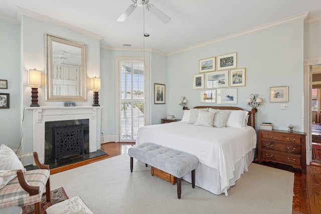 bedroom with a ceiling fan, wood finished floors, a fireplace with raised hearth, and ornamental molding