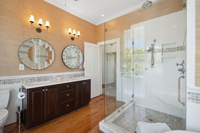 bathroom with a stall shower, toilet, a sink, double vanity, and wood finished floors