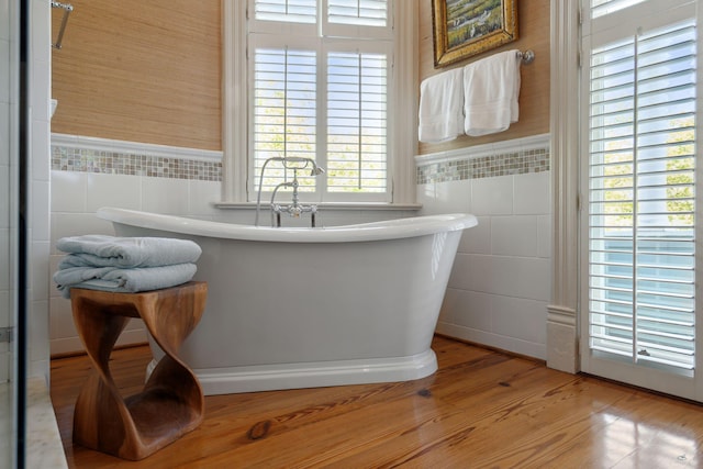 full bath featuring tile walls, wainscoting, wood finished floors, and a freestanding bath