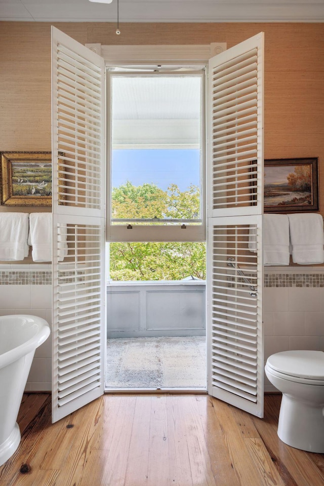 bathroom featuring toilet, tile walls, a soaking tub, and wood finished floors