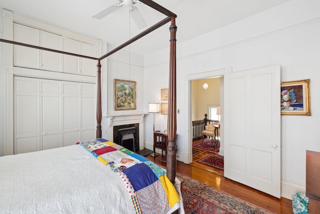 bedroom with a ceiling fan, a closet, baseboards, a high end fireplace, and wood finished floors