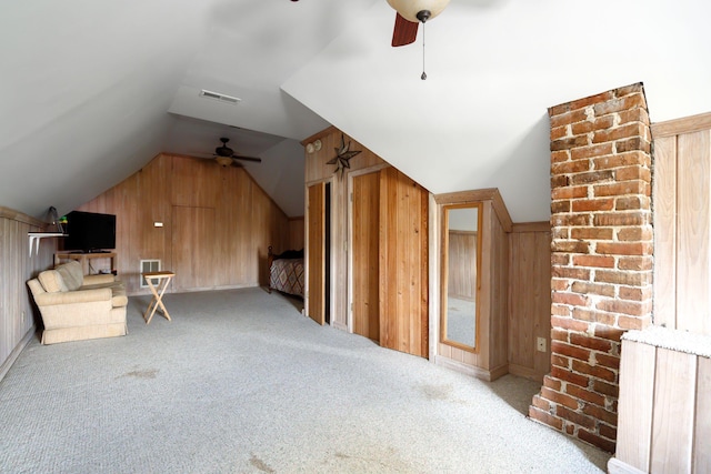 additional living space featuring a ceiling fan, carpet floors, visible vents, wood walls, and vaulted ceiling