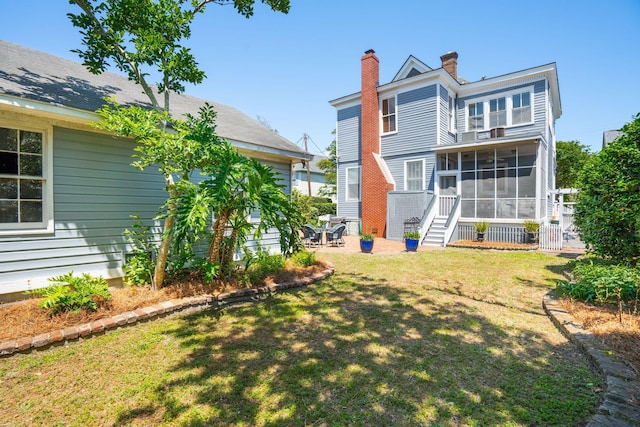 rear view of house featuring a yard, a patio area, a sunroom, and a chimney