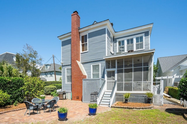 rear view of property featuring a sunroom, a patio, and a chimney
