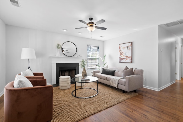 living area featuring a fireplace with flush hearth, wood finished floors, visible vents, and ceiling fan