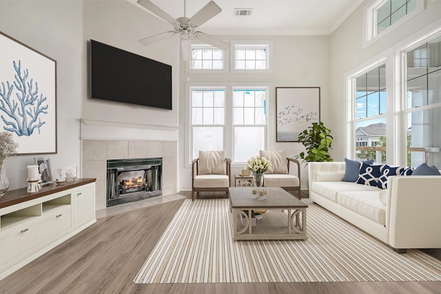130 River Landing Dr Unit 2310, Daniel Island, SC 29492 - living room featuring light wood-style floors, a tiled fireplace, ceiling fan, crown molding, and a high ceiling