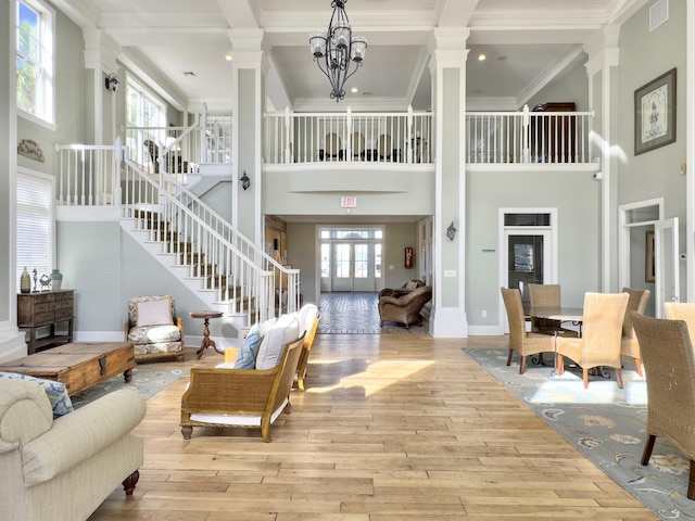 living room with decorative columns, a high ceiling, ornamental molding, a chandelier, and light wood-type flooring