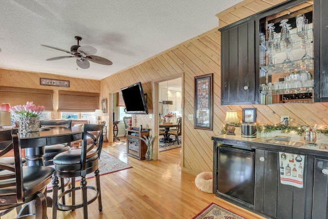 dining space with ceiling fan, a textured ceiling, wood walls, and light hardwood / wood-style floors