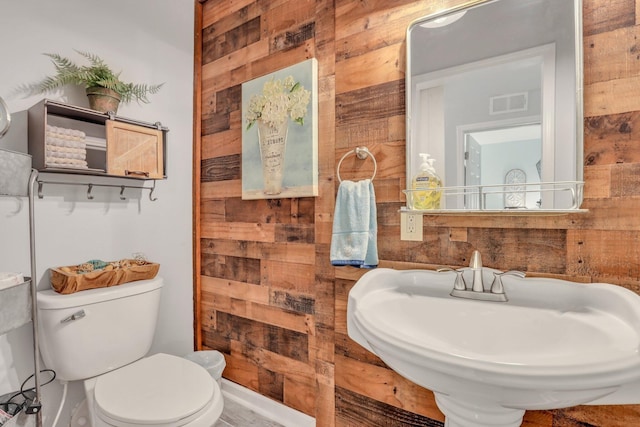 bathroom with sink, wooden walls, and toilet