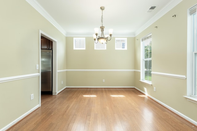 empty room featuring light hardwood / wood-style flooring, crown molding, a wealth of natural light, and a chandelier