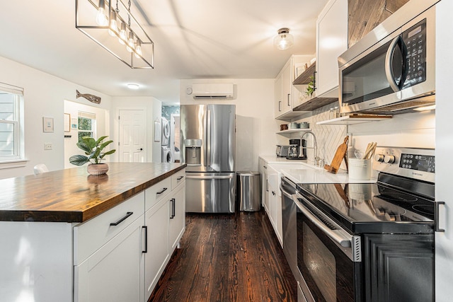 kitchen featuring wooden counters, appliances with stainless steel finishes, an AC wall unit, stacked washer / dryer, and white cabinetry