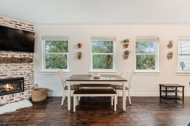 dining area with dark hardwood / wood-style flooring, a wealth of natural light, and a brick fireplace