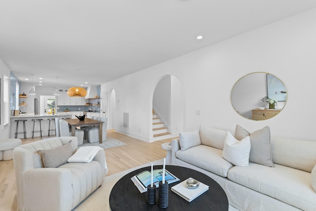 living room featuring arched walkways, light wood-style flooring, recessed lighting, visible vents, and stairway