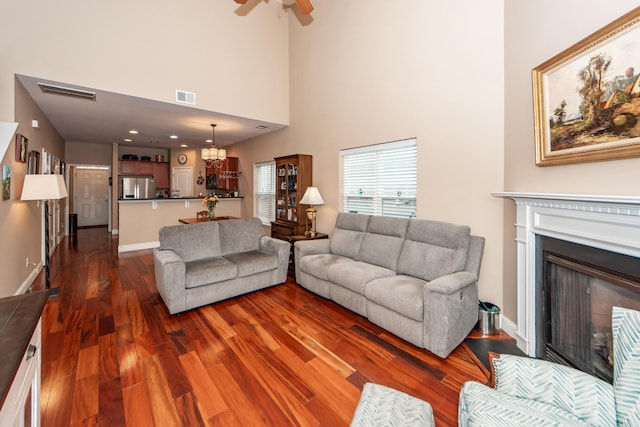 living room with ceiling fan with notable chandelier, a high ceiling, and dark hardwood / wood-style floors