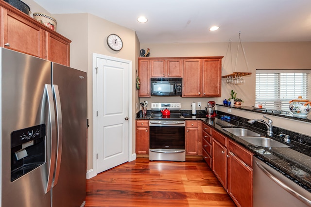 kitchen featuring light hardwood / wood-style flooring, stainless steel appliances, dark stone counters, sink, and decorative light fixtures