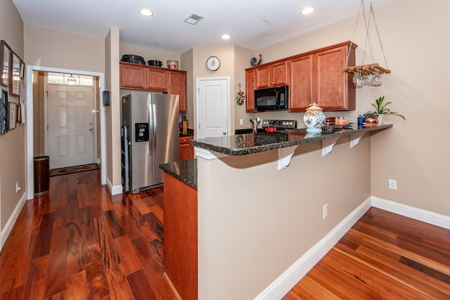 kitchen featuring dark stone countertops, stainless steel appliances, kitchen peninsula, and dark hardwood / wood-style floors