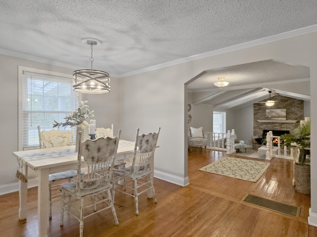 dining space with crown molding, a fireplace, a textured ceiling, and wood finished floors