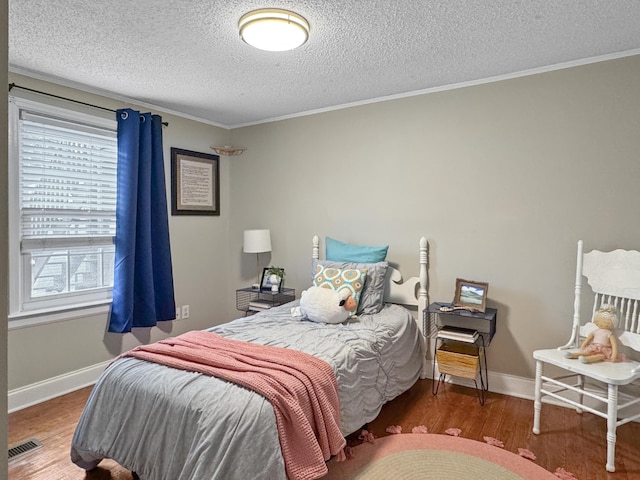 bedroom with baseboards, visible vents, ornamental molding, wood finished floors, and a textured ceiling