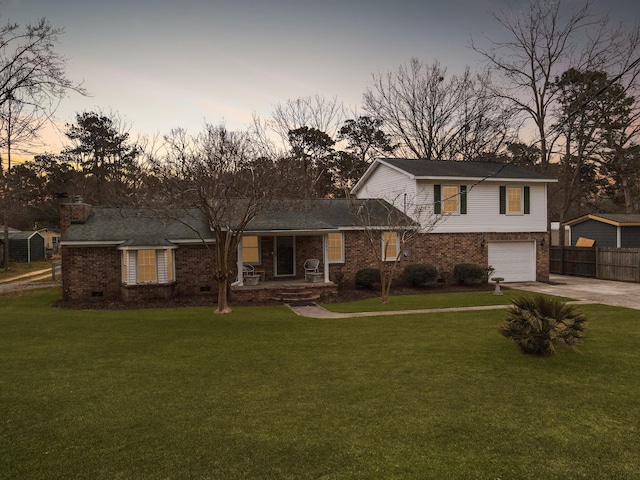 tri-level home with driveway, a garage, a lawn, fence, and brick siding