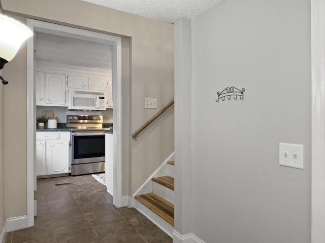 interior space featuring dark tile patterned floors, a textured ceiling, baseboards, and stairs