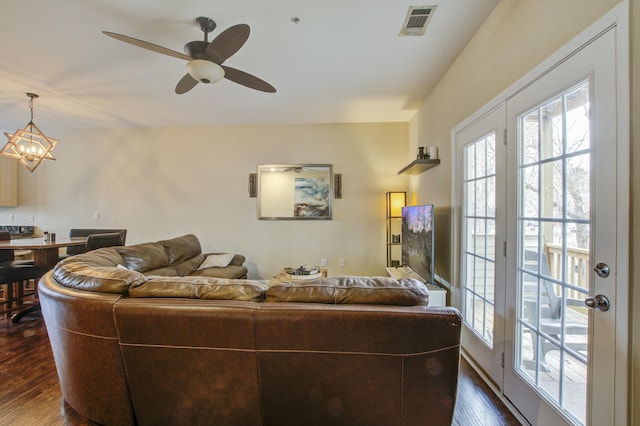 living room featuring ceiling fan with notable chandelier and dark wood-type flooring