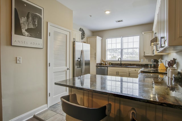 kitchen with appliances with stainless steel finishes, a breakfast bar area, dark stone countertops, and kitchen peninsula