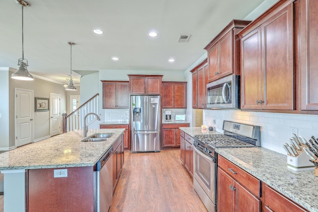 kitchen with light stone countertops, appliances with stainless steel finishes, a sink, light wood-style floors, and decorative backsplash