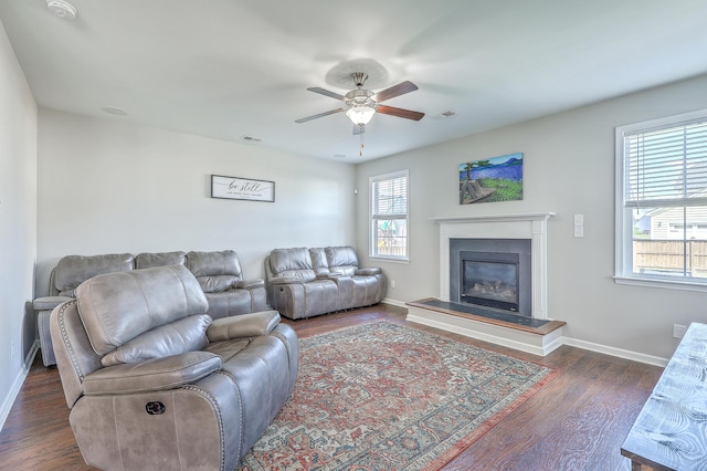 living area featuring ceiling fan, dark wood-style flooring, visible vents, baseboards, and a glass covered fireplace