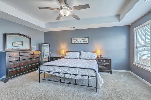 bedroom featuring ceiling fan, carpet floors, baseboards, a tray ceiling, and visible vents
