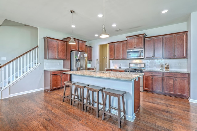 kitchen featuring decorative backsplash, appliances with stainless steel finishes, a sink, a breakfast bar, and dark wood-type flooring