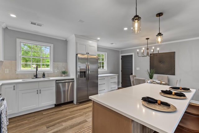 kitchen with appliances with stainless steel finishes, a sink, light wood-style flooring, light countertops, and crown molding