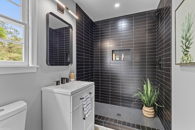 bathroom featuring toilet, vanity, plenty of natural light, tiled shower, and recessed lighting
