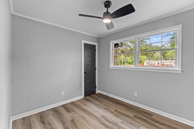 unfurnished room featuring healthy amount of natural light, ceiling fan, wood finished floors, crown molding, and baseboards