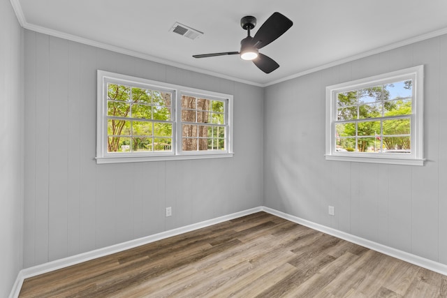 spare room with plenty of natural light, wood finished floors, a ceiling fan, crown molding, and baseboards