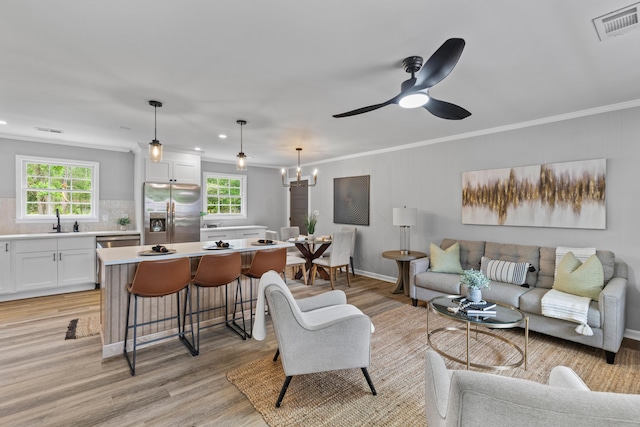 living room featuring healthy amount of natural light, light wood-style flooring, ornamental molding, a chandelier, and a ceiling fan