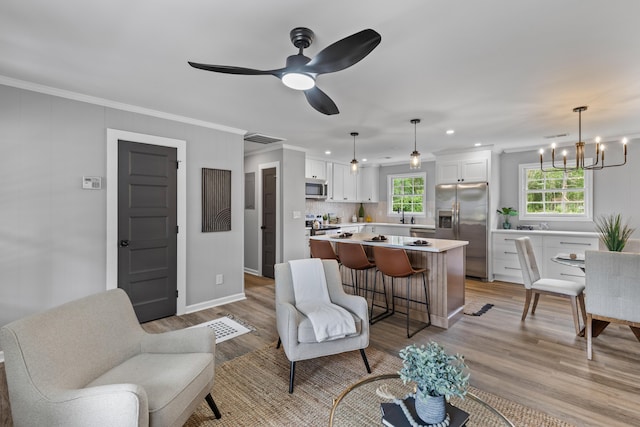 living room featuring a chandelier, light wood-type flooring, crown molding, a ceiling fan, and recessed lighting