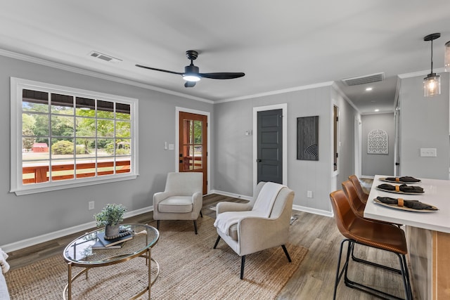 living area with ornamental molding, wood finished floors, a ceiling fan, and baseboards