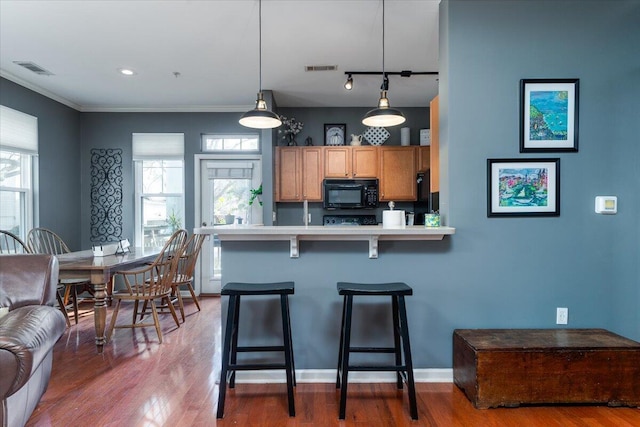 kitchen featuring hardwood / wood-style flooring, a wealth of natural light, a kitchen bar, decorative light fixtures, and kitchen peninsula